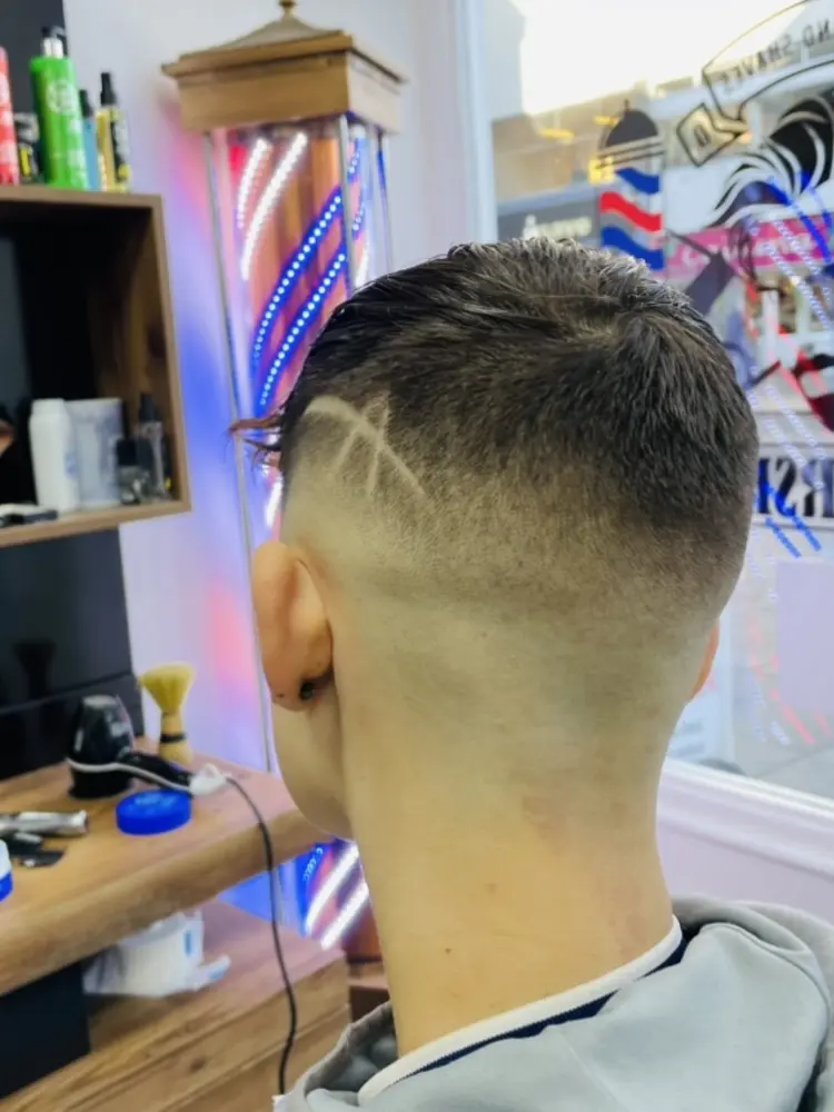 Back of a client's head showing a skin fade with a shaved line design at HB Barbershop