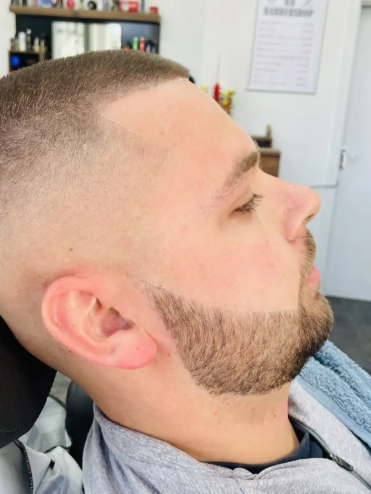 Side profile of a client with a high skin fade and neatly lined beard